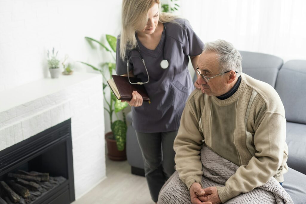 Caring nurse talks to old patient holds his hand sit in living room at homecare visit provide